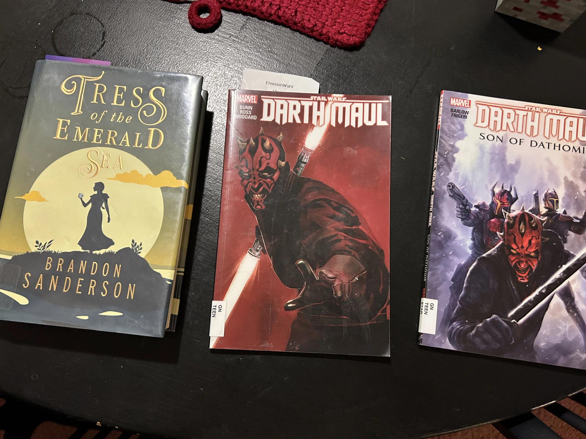 An image of 3 books sitting on a table. The books are 'Tress of the Emerald Sea' by Brandon Sanderson and two Darth Maul graphic novels. The original, and Son of Dathomir.